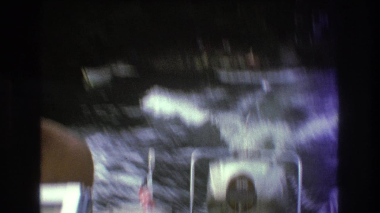 A blurred 8mm frame shows lake wake, spray, a partial adult figure, and boat hardware during the Boston-area waterskiing attempt.