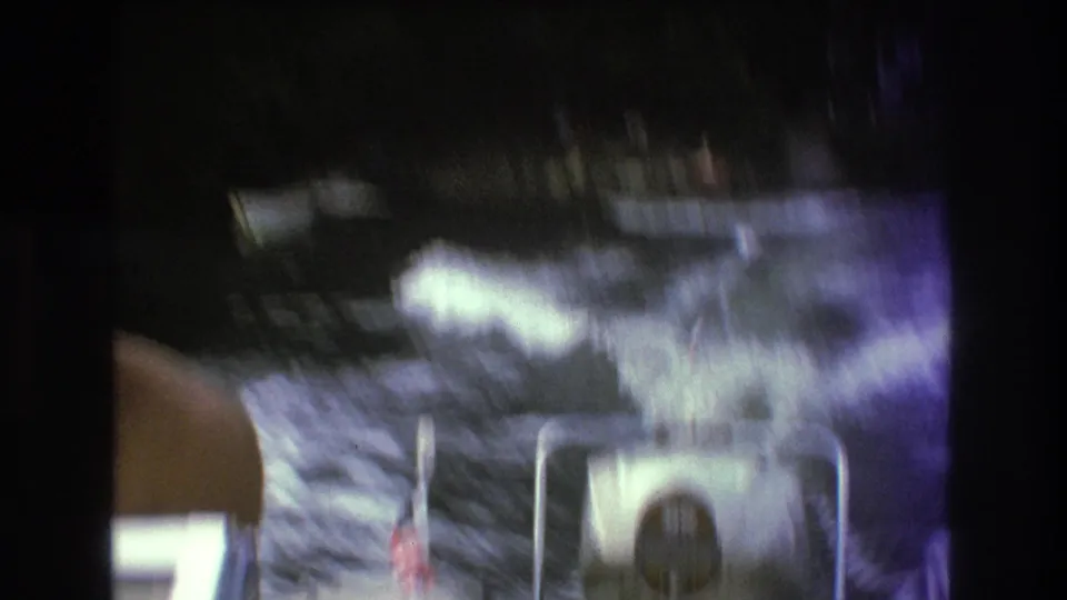 A blurred 8mm frame shows lake wake, spray, a partial adult figure, and boat hardware during the Boston-area waterskiing attempt.