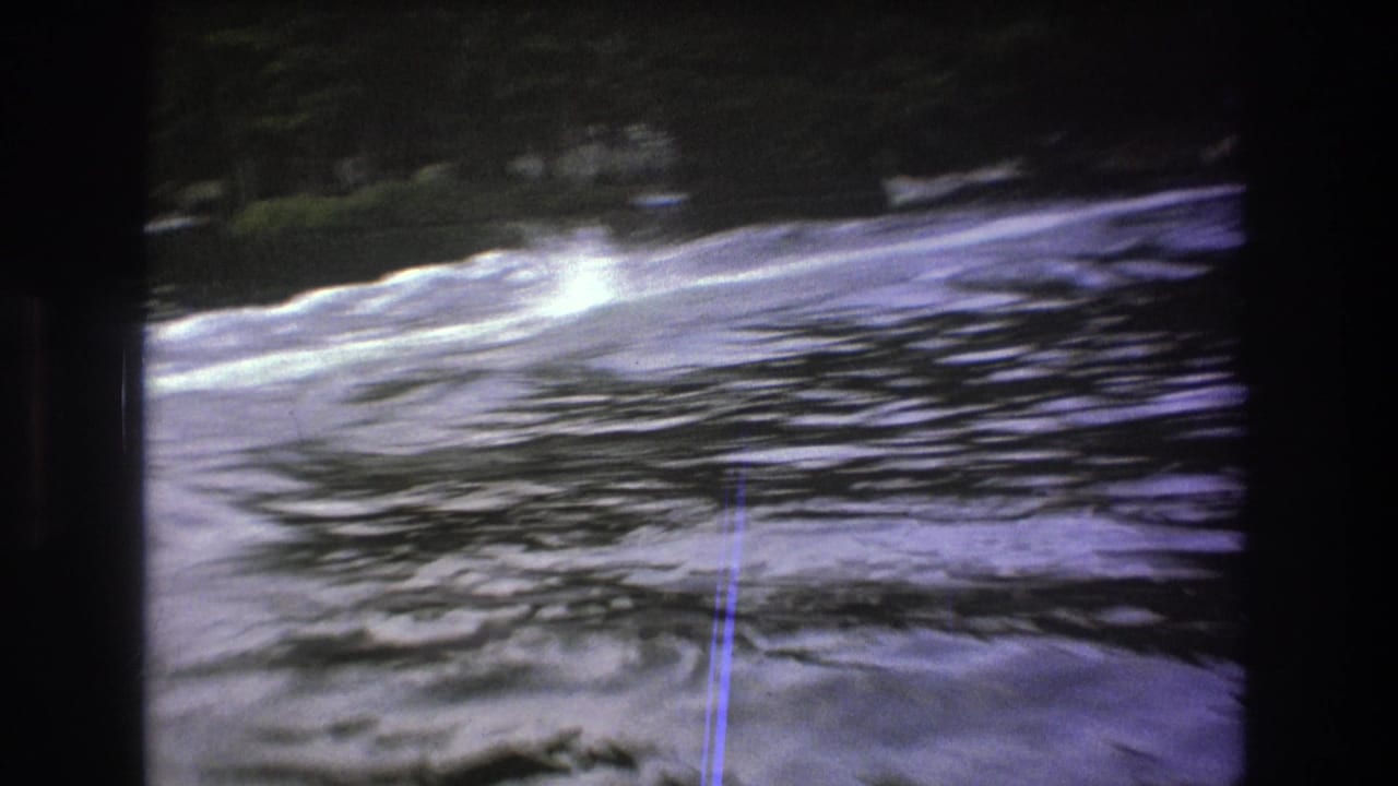 Foamy wake crosses the lake surface in a soft, grainy 1975 8mm Boston-area frame, with trees along the far shore.