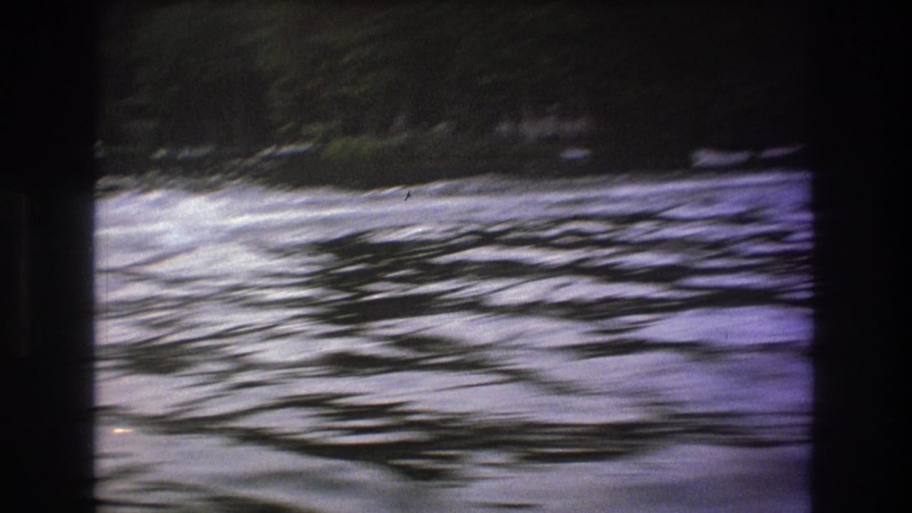1975 8mm home-movie frame showing rippled river water and a wooded bank, with no boat clearly visible in this moment.