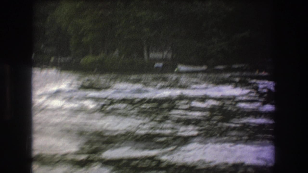 1975 8mm home-movie frame with motion-blurred whitewater and a tree-lined riverbank as the boat moves out of view.