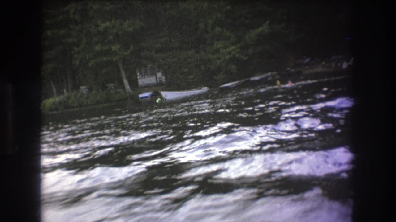 1975 8mm home-movie frame showing a small boat near the far wooded bank as whitewater moves across the foreground.