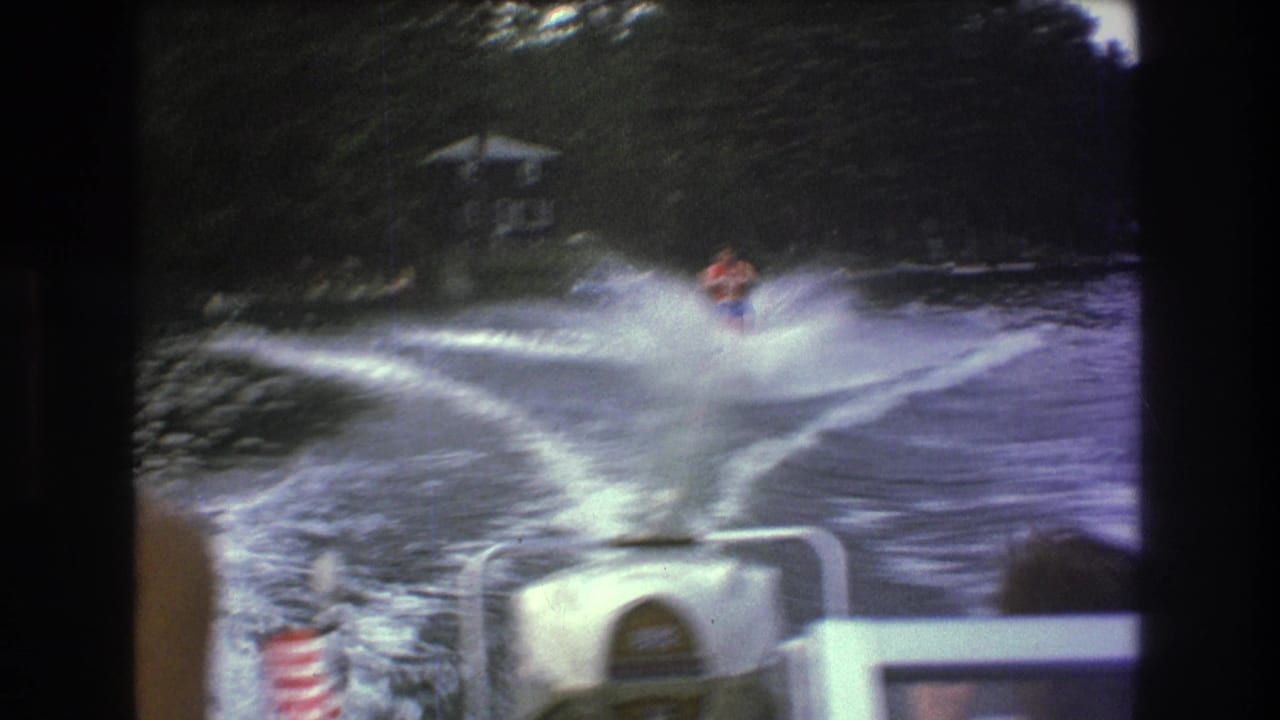 Water skier arcs across the wake behind a boat near a wooded shoreline.