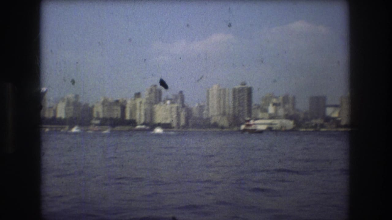 Boston waterfront buildings and a vessel near the shore, captured in grainy 1975 8mm footage with visible dust marks.
