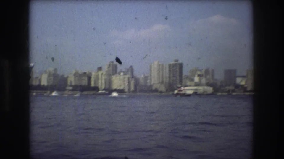 Boston waterfront buildings and a vessel near the shore, captured in grainy 1975 8mm footage with visible dust marks.