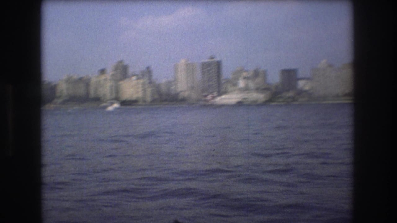 Soft 8mm view of Boston in 1975 from the harbor, showing a distant skyline, small boats, and broad water in the foreground.