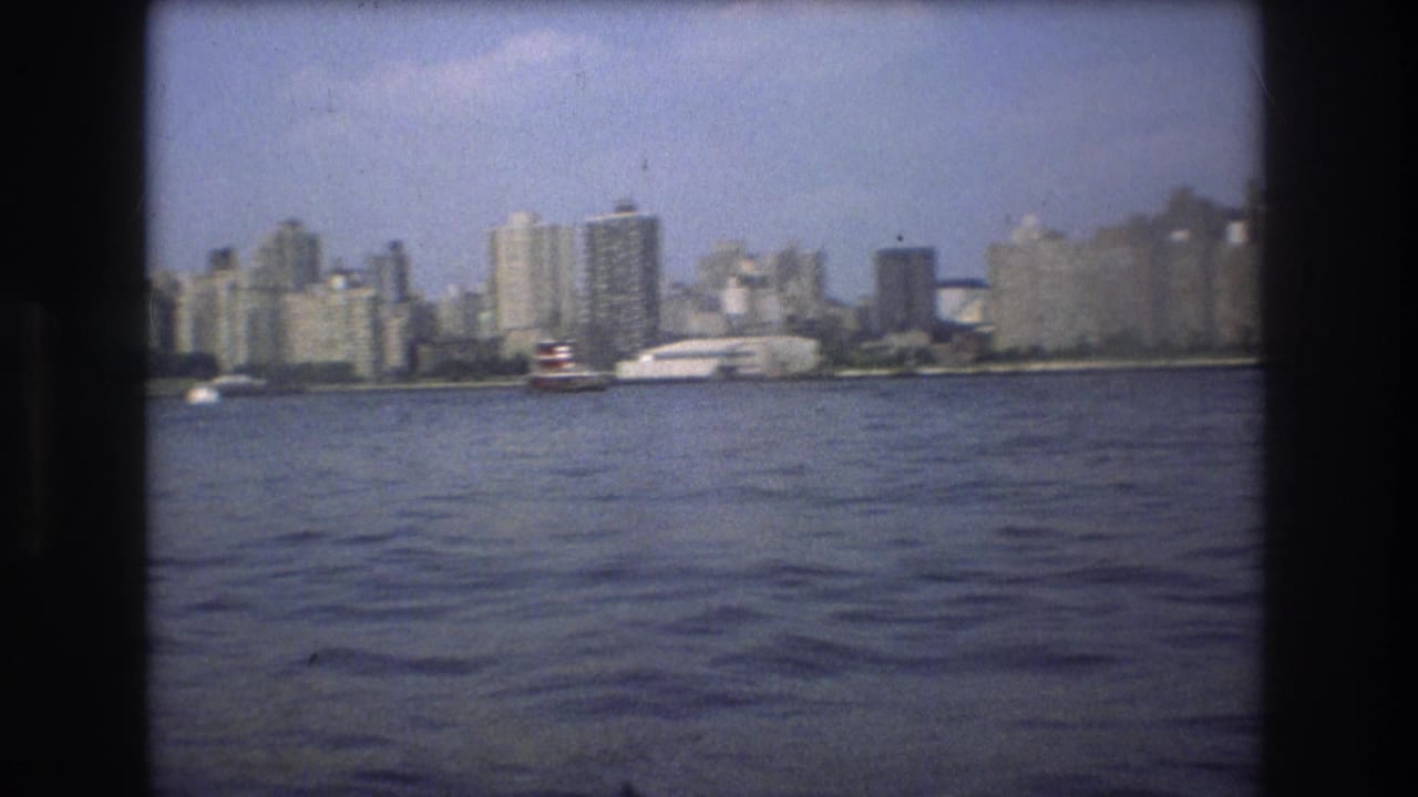 Soft 8mm frame from Boston in 1975 showing a boat on the harbor before a hazy skyline of waterfront high-rises.