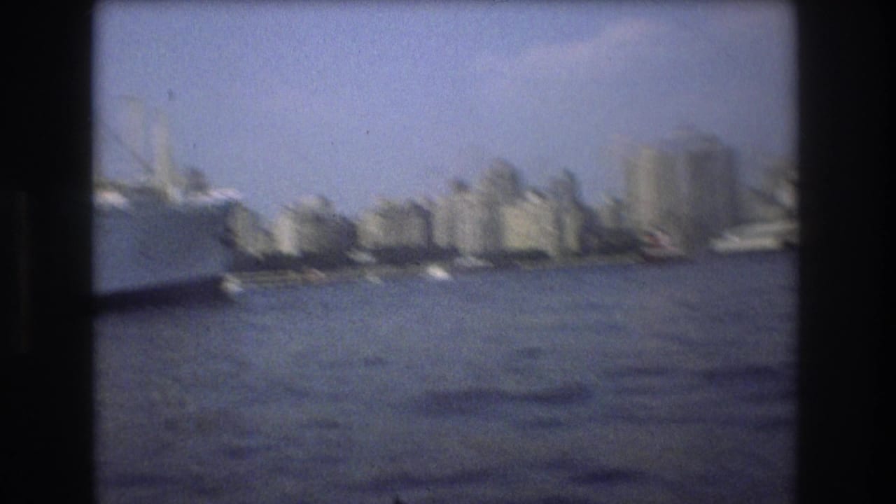 Soft 8mm frame of Boston harbor in 1975 showing the city skyline across the water and a large vessel partly entering from the left edge.