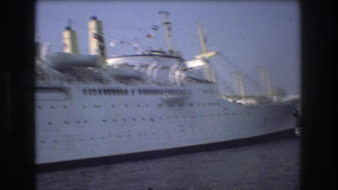 Large white ship in Boston harbor in 1975, seen close to frame with smokestacks, deck structures, and harbor cranes in the background.
