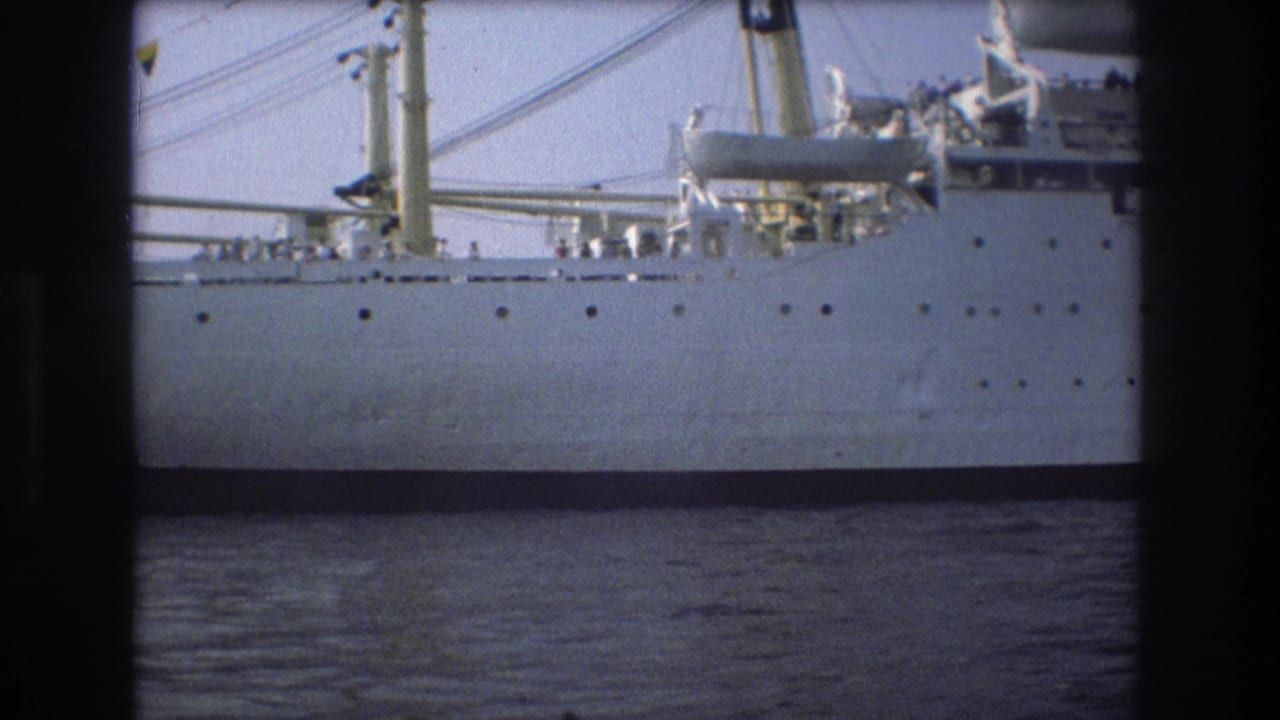 Side view of the large white ship in 1975 Boston harbor, showing hull portholes, mast rigging, deck equipment, and water at the bottom of frame.