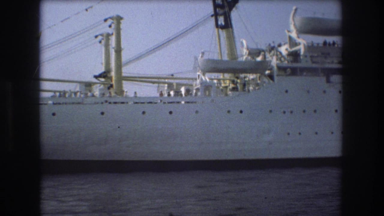 1975 Boston 8mm frame showing the side of a large white ship on harbor water, with rows of portholes, davits, deck gear, and small figures visible near the rail.