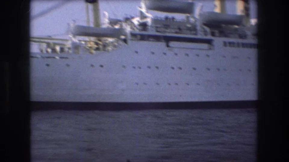 1975 Boston 8mm frame with a closer view of the ship's white hull, porthole rows, lifeboat equipment, upper deck, and dark water beneath.