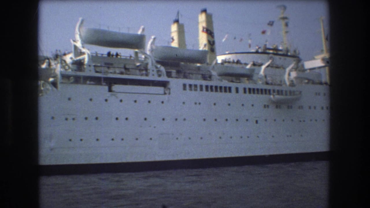 1975 Boston 8mm frame showing the midsection of a large white ship with twin funnels, lifeboats, portholes, railings, and passengers or crew gathered on deck.