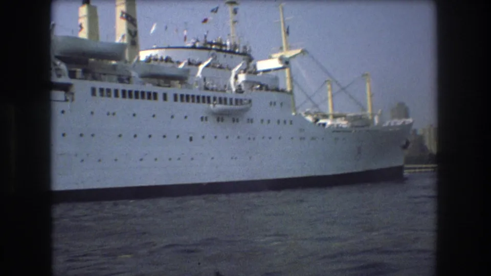 A large white passenger ship with decks, lifeboats, and cranes appears on Boston harbor water in the supplied 1975 home-movie clip.