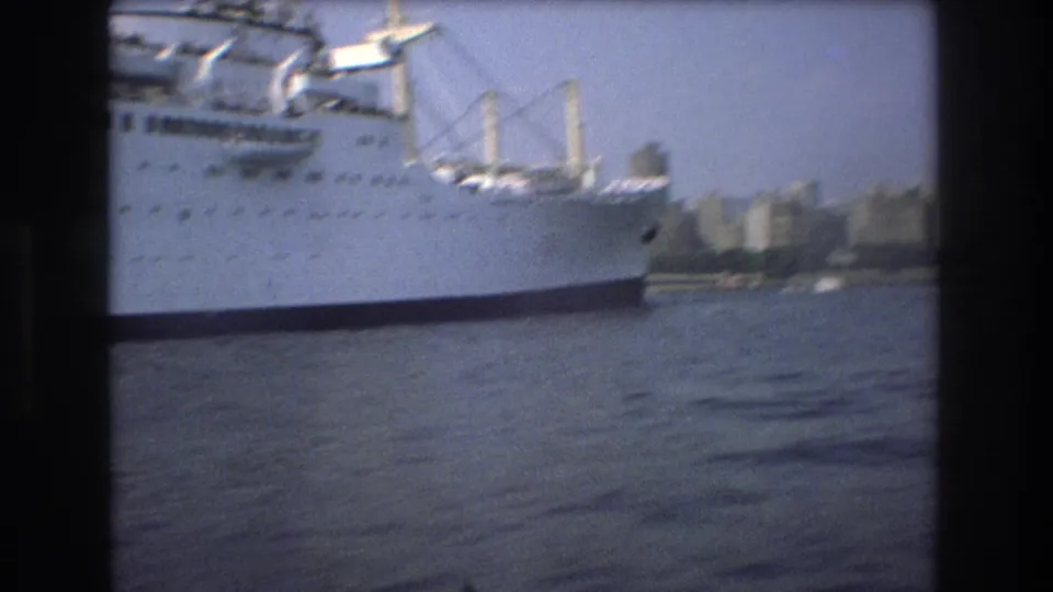 The white passenger ship continues across the harbor, partly framed by 8mm contact-sheet borders with water and a distant shoreline behind it.