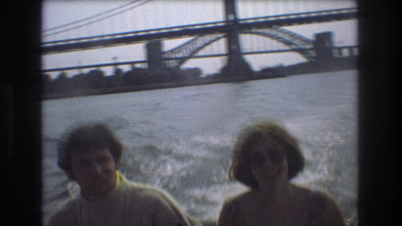 Man and woman on a boat with water wake and bridge spans in the background.
