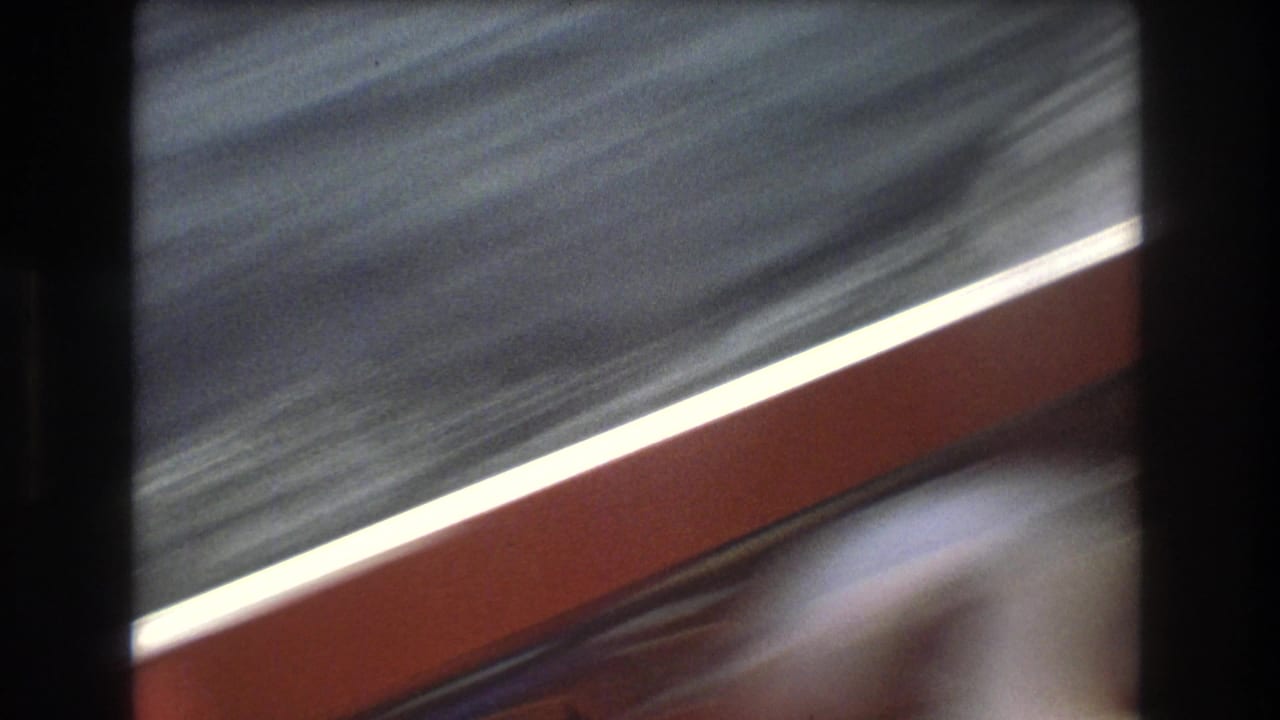 Soft, motion-blurred 1975 Boston home-movie frame from a small boat, showing choppy water, a red-edged rail or seat, and a partial foreground figure or object.
