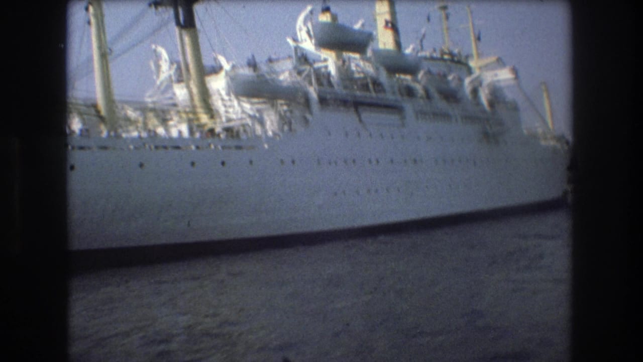 Closer 1975 Boston harbor view of a large white passenger ship, showing the hull, rows of small windows, upper deck structures, and rippled water from a moving small-boat viewpoint.