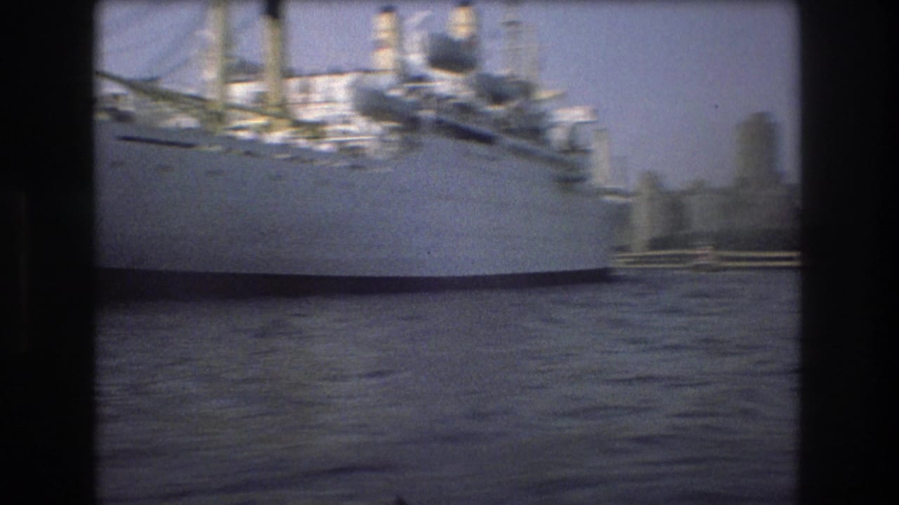 1975 Boston Harbor home-movie frame showing a large white ship at left, rippled water, and a distant waterfront skyline.