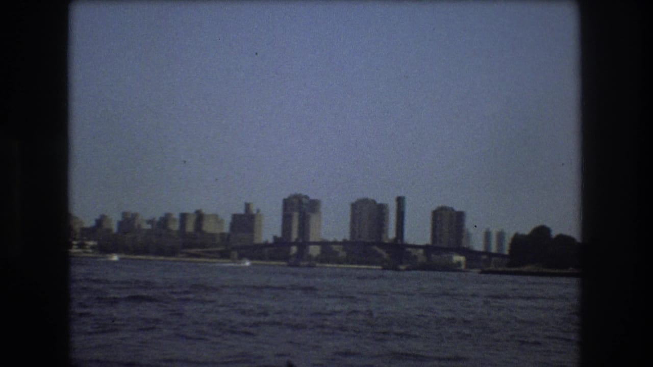 1975 Boston home-movie frame showing a bridge spanning the waterfront with distant towers and open water in the foreground.