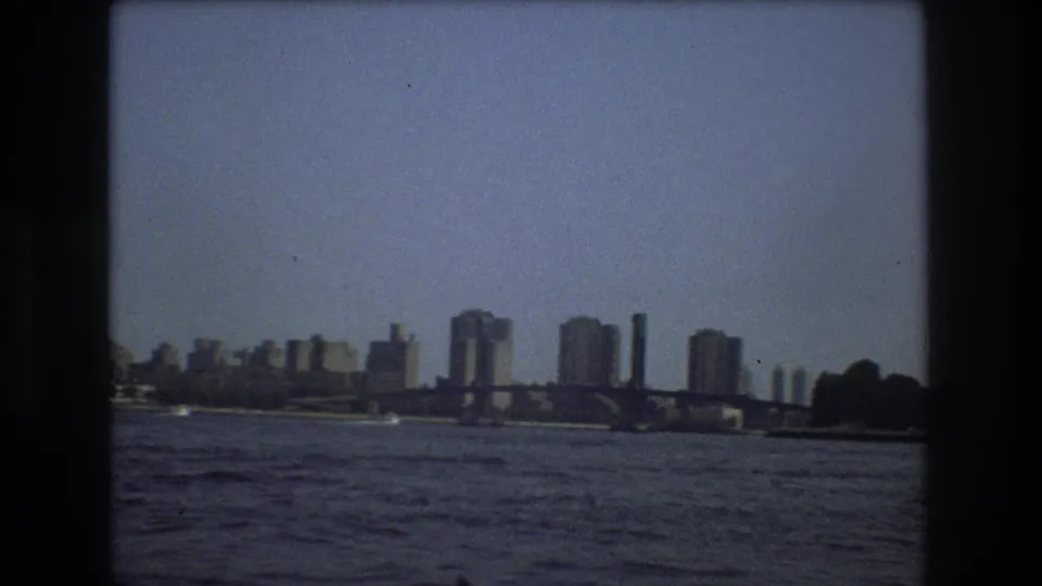 1975 Boston home-movie frame showing a bridge spanning the waterfront with distant towers and open water in the foreground.