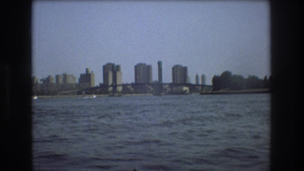1975 Boston harbor view from a small boat, with open water in the foreground, a low bridge, and distant city buildings along the waterfront.