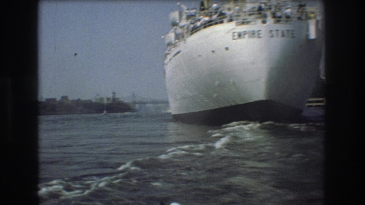 The white bow of the vessel named Empire State fills the right side of this 1975 Boston harbor frame, with small figures visible on the deck and water wake below.