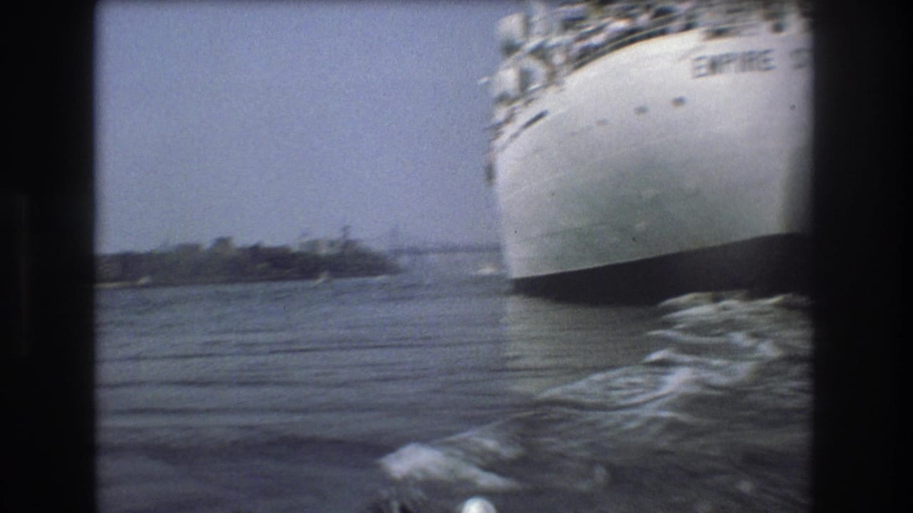 1975 Boston harbor home-movie frame showing the bow of the white Empire State vessel from a nearby boat, with water wake and distant shoreline visible.