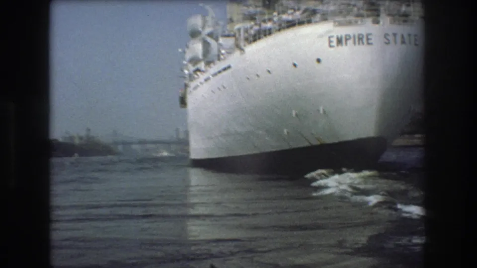 1975 Boston harbor frame with the Empire State name readable on the white hull as the vessel passes near the camera over rippled water.