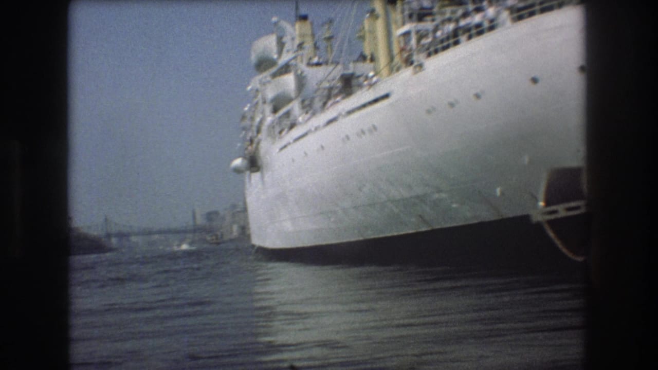 1975 Boston harbor frame showing the Empire State vessel close to the camera, with the curved white hull, deck equipment, water reflection, and hazy background structures visible.