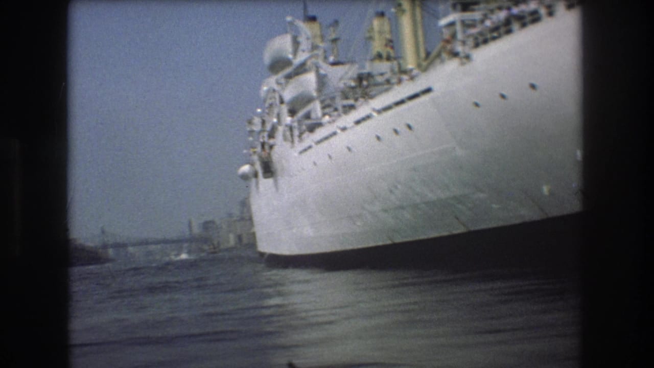 1975 Boston harbor home-movie frame showing the bow and hull of a large white ship from a low small-boat viewpoint on the water.