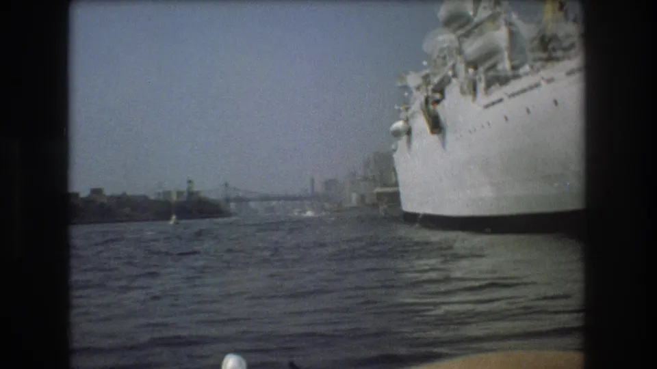 1975 Boston harbor frame with a large white ship partly cropped at right, rippled water in the foreground, and distant shoreline beyond.