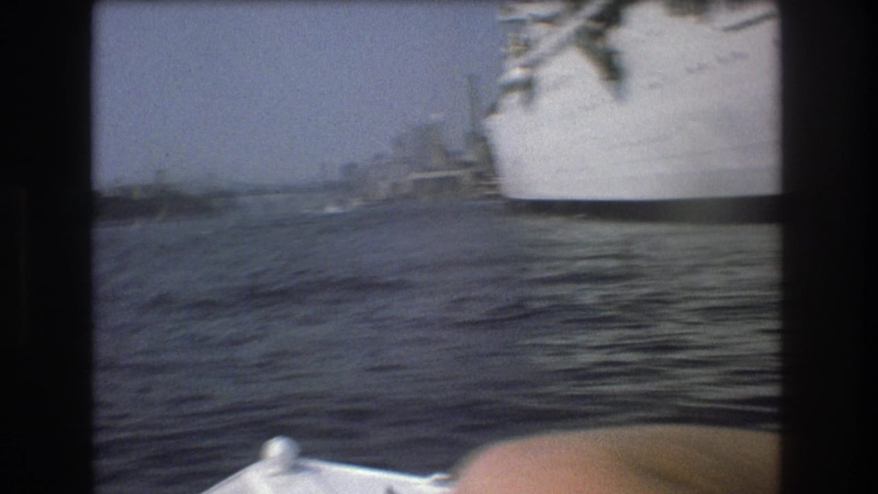 1975 Boston harbor frame from a small boat, with a large white ship cropped along the right side and rippling water across the foreground.
