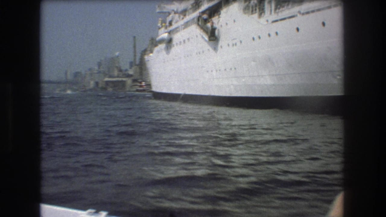 1975 Boston home-movie frame showing a large white passenger ship close to the camera, choppy harbor water, and distant port structures.