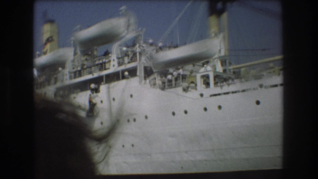 1975 Boston harbor 8mm frame showing a large white passenger ship at a pier, with small figures visible along the decks and dark boat-window framing at the edges.