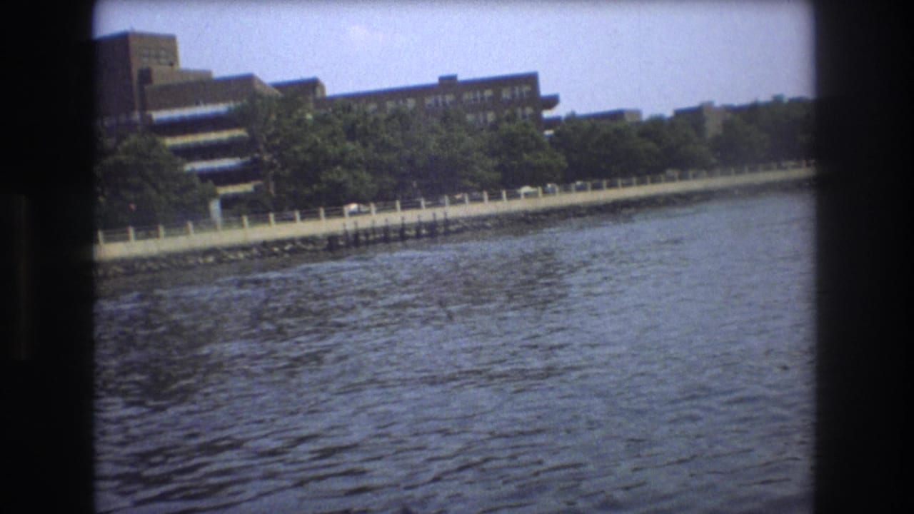 Boston waterfront buildings and a tree-lined shoreline appear across rippling water in 1975 8mm home-movie footage shot from a boat.