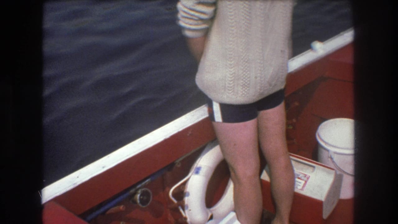 1975 Boston 8mm frame with a rear view of a person standing at the red boat rail, with dark water and a white life preserver visible nearby.