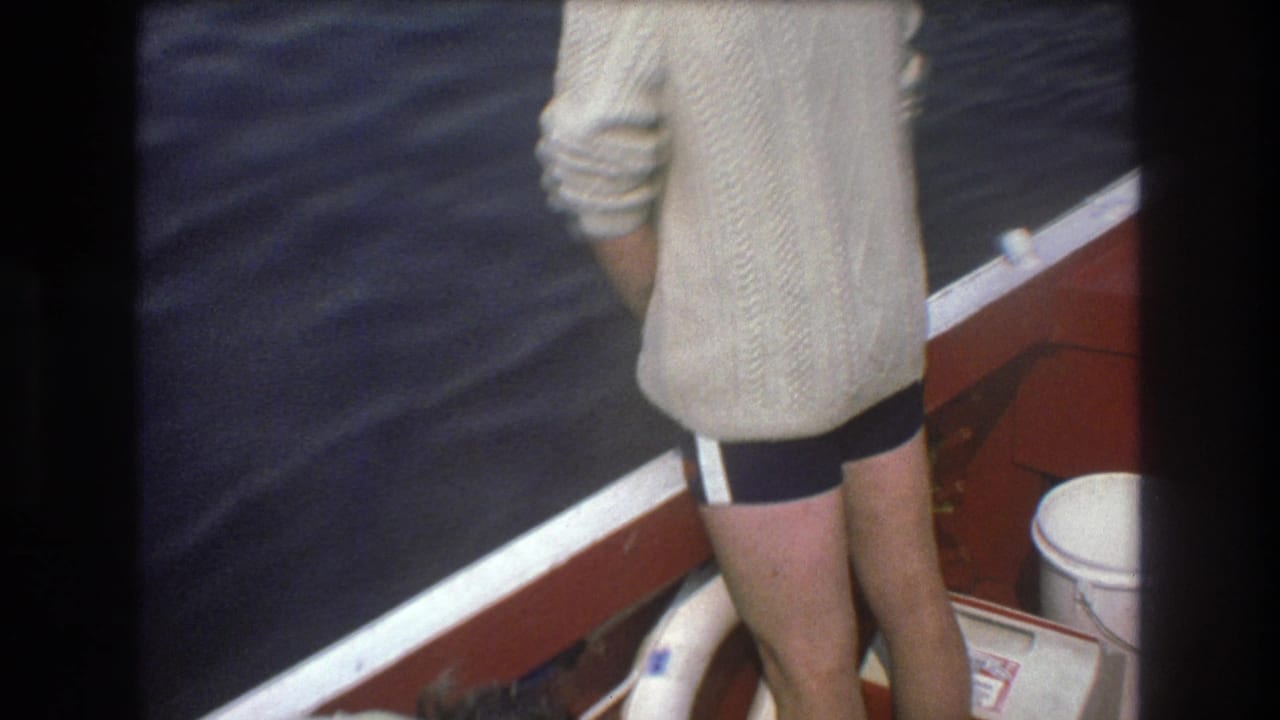 1975 Boston 8mm frame showing a person from behind near the red boat rail, with dark rippling water, a white life preserver, and deck fittings in view.