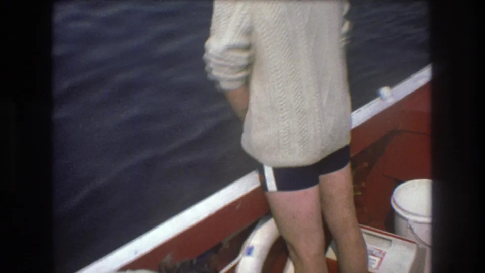 1975 Boston 8mm frame showing a person from behind near the red boat rail, with dark rippling water, a white life preserver, and deck fittings in view.