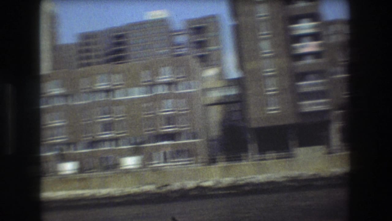 Motion-blurred 8mm view of Boston waterfront apartment facades, balconies, and shoreline passing quickly as the boat moves along the water.