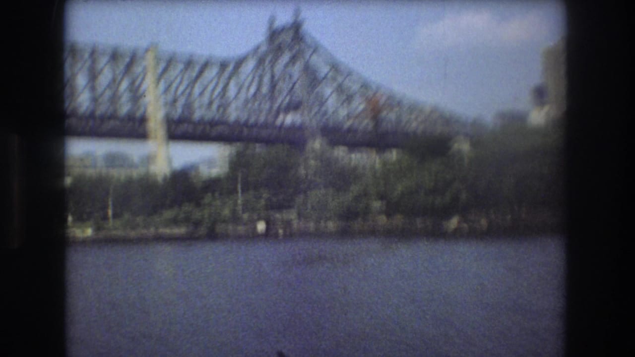 1975 Boston 8mm frame showing a steel truss bridge over a river, with shoreline trees and soft dark film edges.