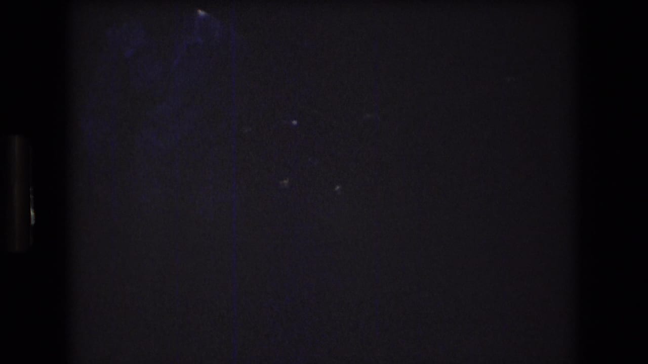 Dark, underexposed 8mm frame from the start of the 1976 Mt Bromley clip, with faint blue-toned shapes and heavy grain but no clear subject visible.