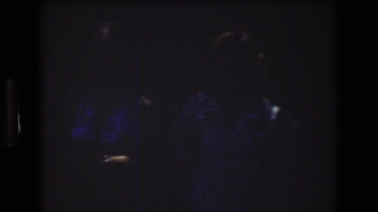 Very dark frame with faint blue shapes and small bright highlights.