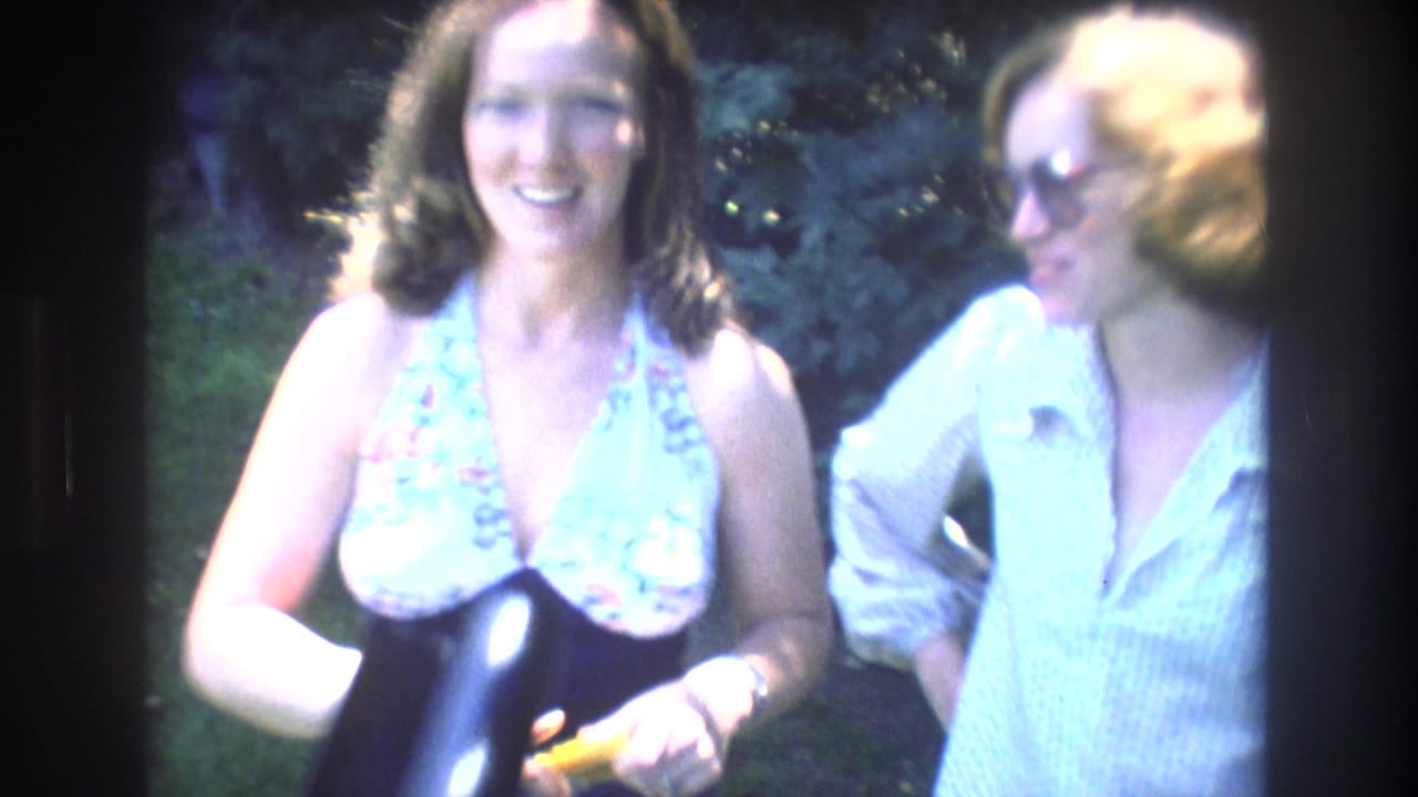 Two adult women stand outdoors at Mt Bromley, Vermont in 1976, one smiling toward the camera in a floral halter top and the other wearing sunglasses and a light blouse beside leafy greenery.
