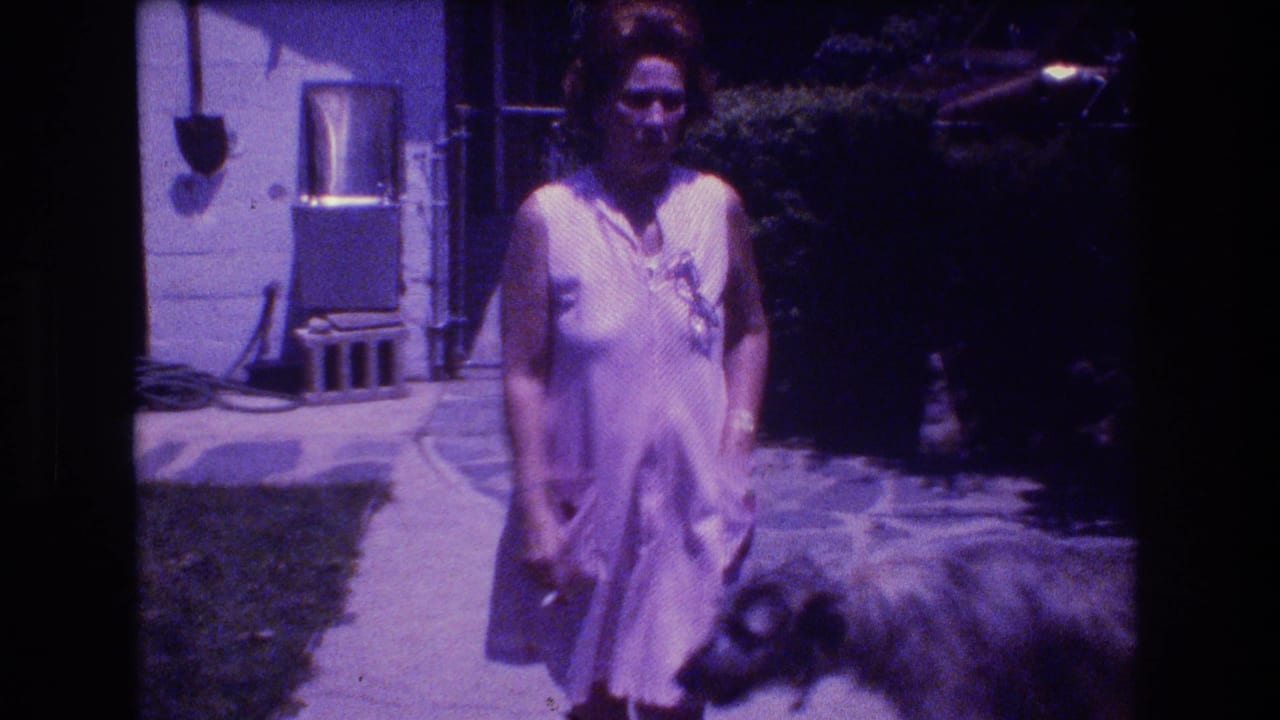 Woman in a light sleeveless dress stands on a backyard path near a dog and house exterior.
