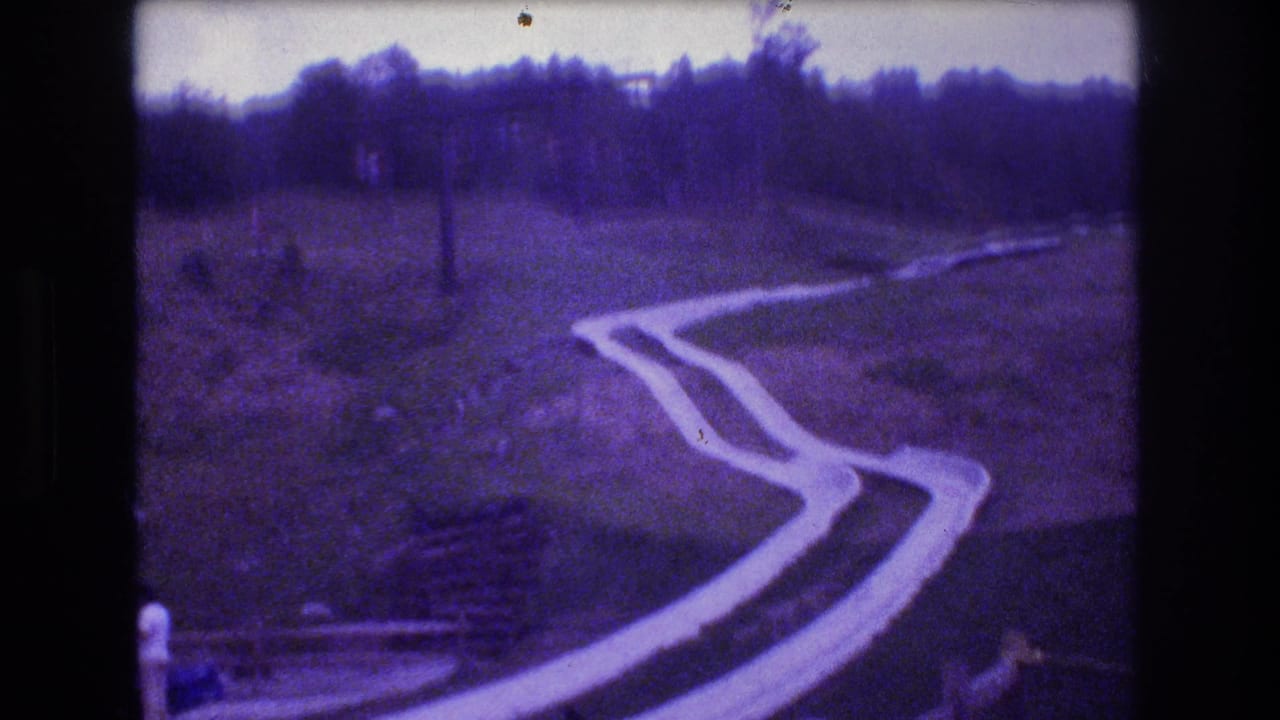 1976 Mt Bromley, Vermont home-movie frame showing a winding concrete slide running down a grassy hillside below a wooded tree line.