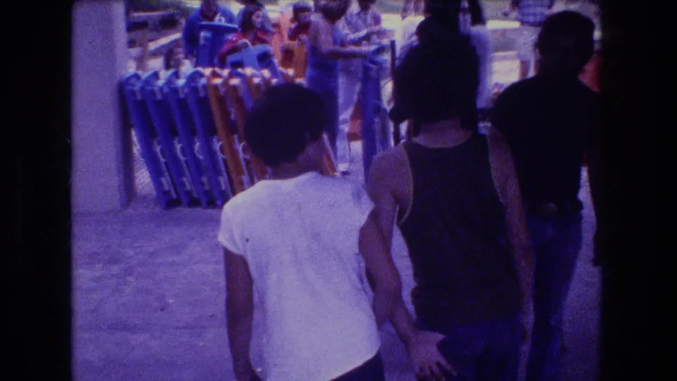 1976 Mt Bromley 8mm frame showing visitors from behind near stacked folding chairs and a walkway area, with the shot retaining the reel's purple color cast.