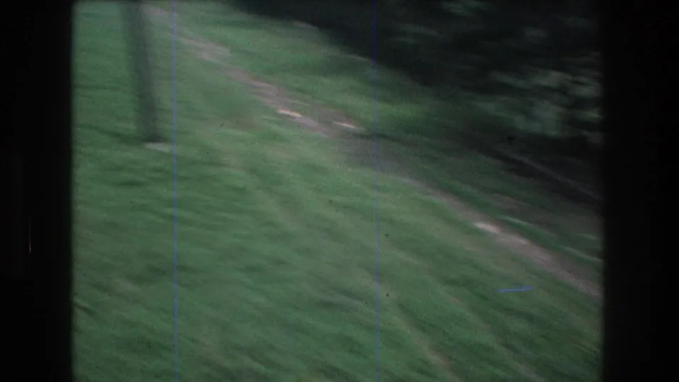 Motion-blurred 8mm frame from the moving lift, with the grassy Mt Bromley slope and a pale trail passing below.