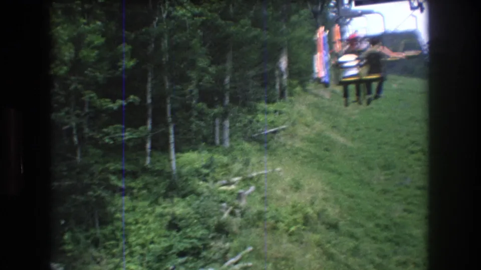 A slightly blurred Super 8 frame shows the chairlift continuing uphill at Mt Bromley, with passengers passing over grass near dense trees.