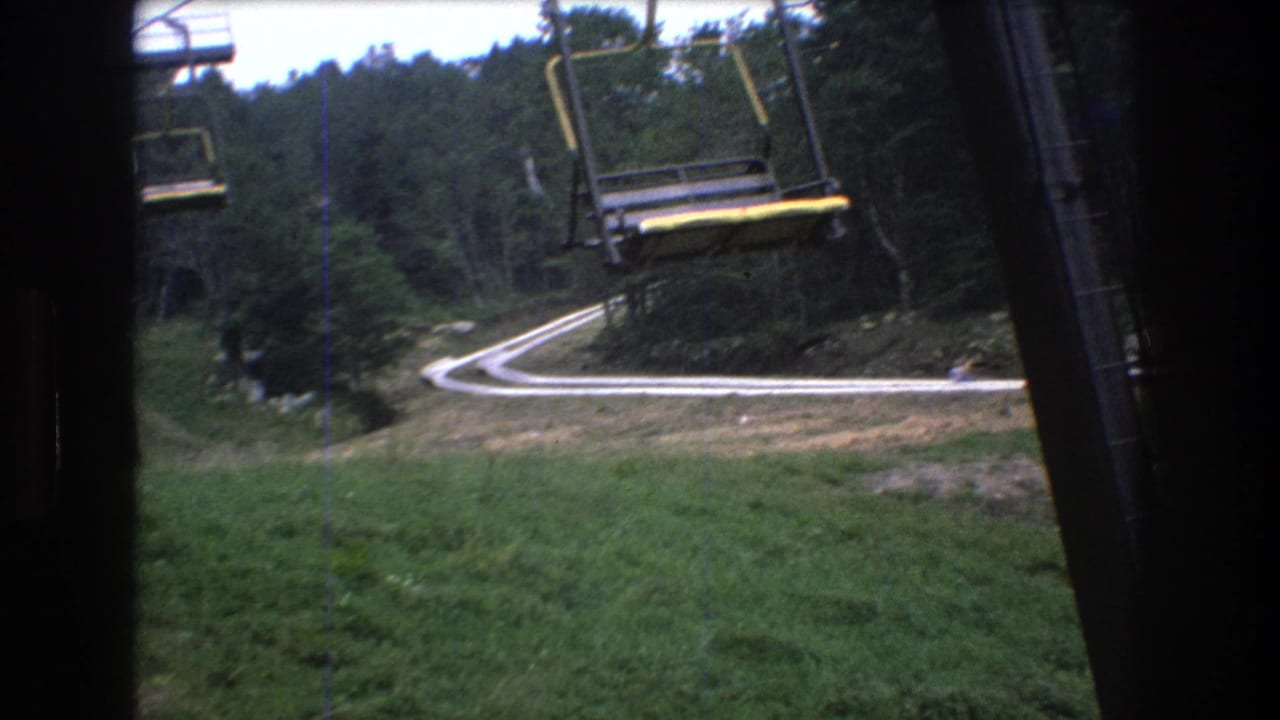 Chairlift chairs hang above a curved road through a wooded hillside.